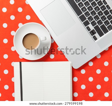 Cup of coffee and notebook near laptop computer on red polka dot background
