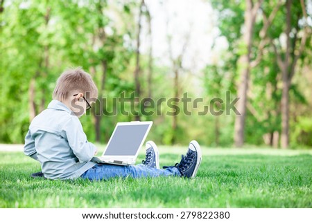 young boy with a books and laptop computer on green grass in the park