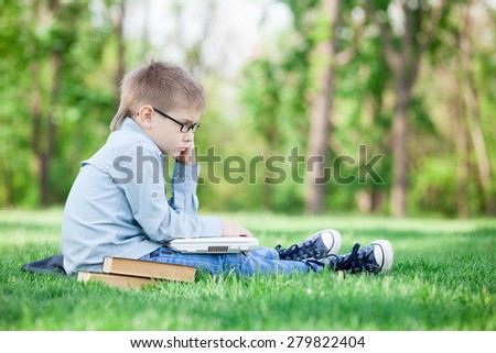 young boy with a book and laptop computer on green grass in the park
