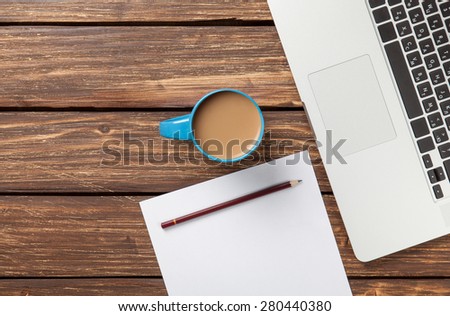 Cup of coffee and paper with laptop computer on wooden background