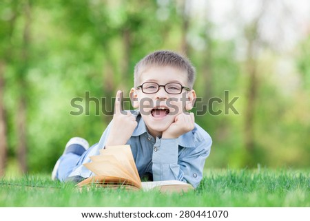 young boy with a book on green grass in the park
