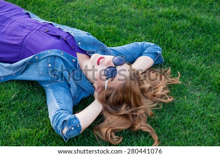 Beautiful blonde women lying down on green grass in summer time in the park.