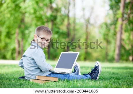 young boy with a books and laptop computer on green grass in the park