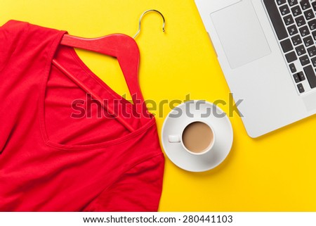 Cup of coffee and laptop computer near red dress on yellow background