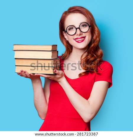Young redhead student in red dress with books on blue background.