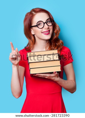 Young redhead student in red dress with books on blue background.