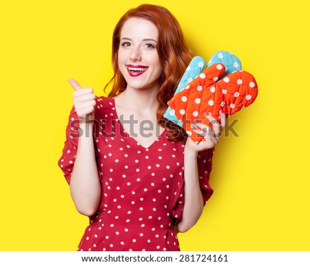 Smiling redhead girl in red polka dot dress and mittens on yellow background.