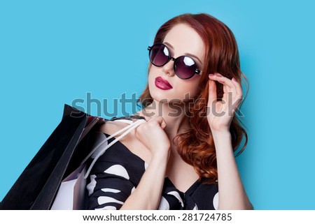 Redhead girl in black dress with shopping bags on blue background
