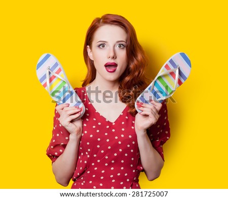 Surprised redhead girl in red polka dot dress with flip flops on yellow background.