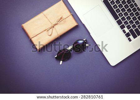 Vintage package and laptop computer with glasses on violet background.