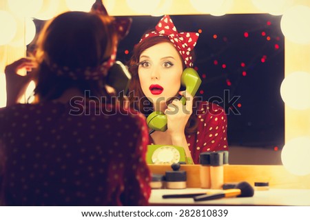 Portrait of a beautiful surprised woman with a dial phone and applying cosmetics near a mirror. Photo in retro color style.