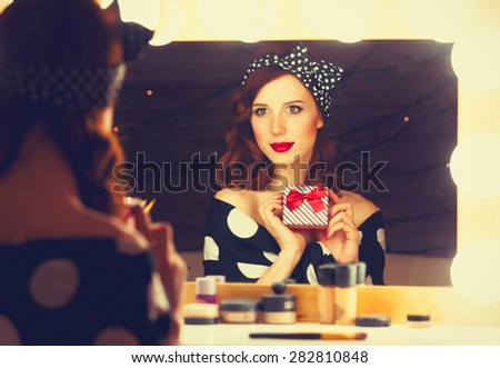 Portrait of a beautiful smiling woman with present box near a mirror. Photo in retro color style.