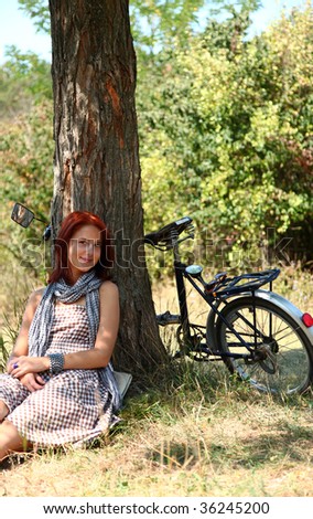 Beautiful girl sitting near bike and tree at rest in forest.