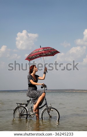 Girl go for a cycle ride at water with umbrella in hand.