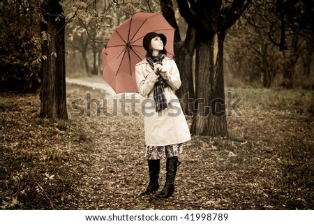 Girl in cloak and scarf with umbrella at park in rainy day. Photo in vintage style with nature colour.
