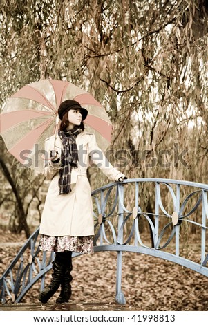 Girl in cloak and scarf with umbrella at park in rainy day. Photo in vintage style with nature colour.
