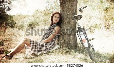 Beautiful girl sitting near bike and tree at rest in forest. Photo in old colour image style.