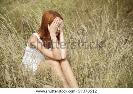 Sad red-haired girl at grass. Outdoor photo.