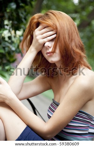 Sad red-haired girl at garden. Outdoor photo.