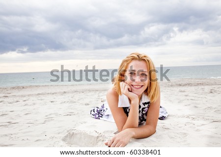 Beautiful blonde girl lying on sand at the beach in rainy day.