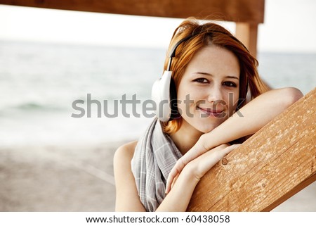 Portrait of young red-haired girl in headphone near wood at beach.