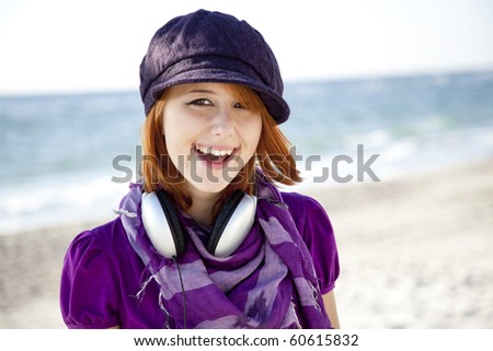 Portrait of red-haired girl in cap with headphone on the beach.