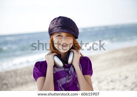 Portrait of red-haired girl in cap with headphone on the beach.