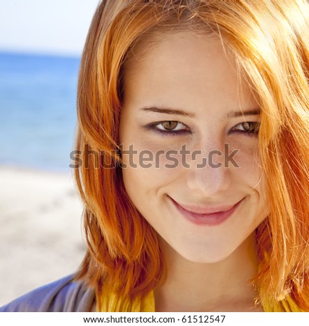Close-up portrait of red-haired girl at outdoor with blue sea at background.