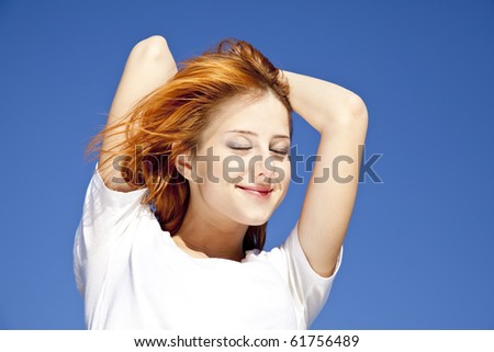 Portrait of red-haired girl in white on blue sky background.