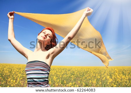 Young woman with open arms keep yellow silk on wind at rapeseed field. Shine from left corner.