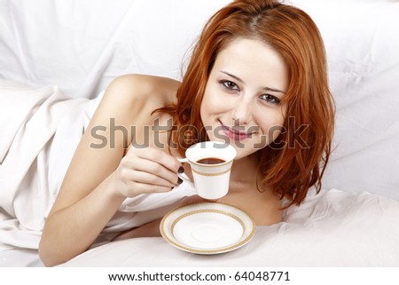 Pretty red-haired woman in white nightie lying in the bed near cup of coffee