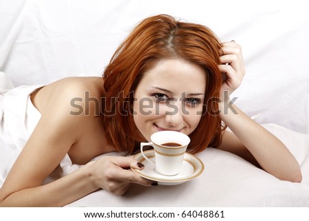 Pretty red-haired woman in white nightie lying in the bed near cup of coffee