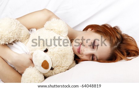 Pretty red-haired sleeping woman in white nightie lying in the bed with soft toy.