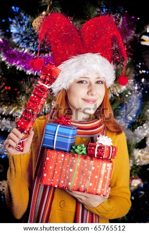 Funny girl in christmas cap with gift boxes and  tree at background.
