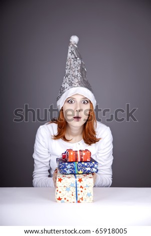 Surprised red-haired girl in christmas cap with gift boxes.