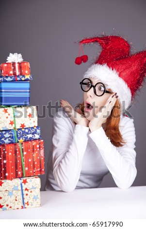 Funny red-haired girl in christmas cap and glasses with gift boxes.