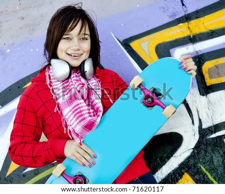 Closeup portrait of a happy young girl with skateboard and graffiti on background