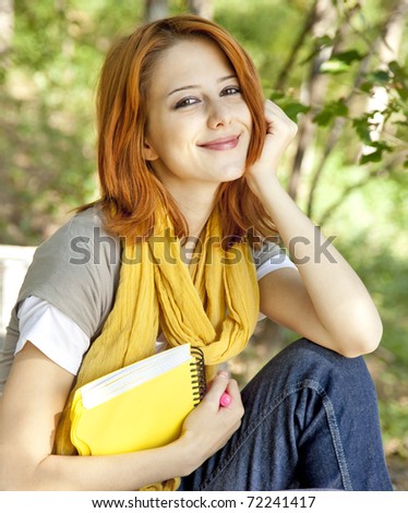 Red-haired student girl with notebook sitting at outdoor.