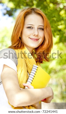 Red-haired student girl with notebook sitting at outdoor.