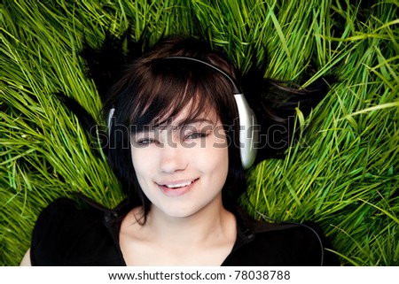 Brunette girl listening music at green grass.