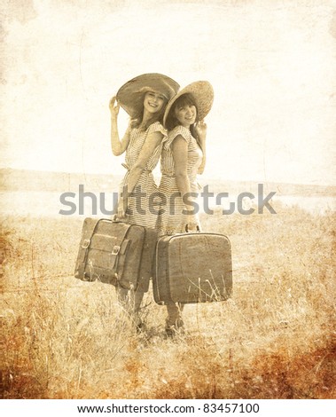 Two retro style girls with suitcases at countryside. Photo in old image style.