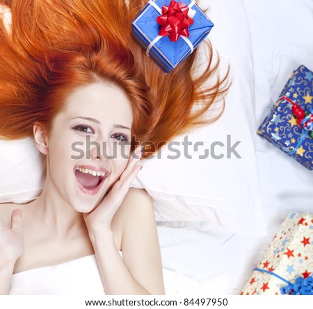 Happy red-haired girl in bed with Christmas gifts. Studio shot.