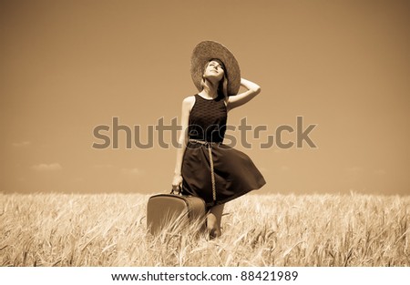 Girl with suitcase at summer wheat field. Photo in old yellow color image style.