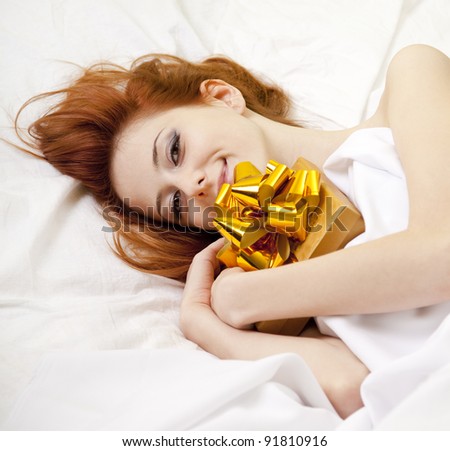 Red-haired girl in bed with gift. Studio shot.