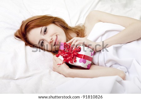 Red-haired girl in bed with gift. Studio shot.