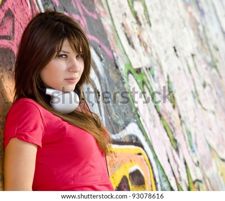 Beautiful brunette girl with headphones and graffiti wall at background.