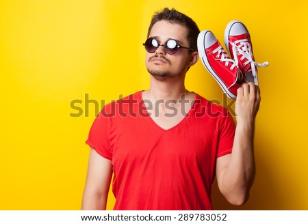 young guy in t-shirt with sunglasses and red gumshoes on yellow background.