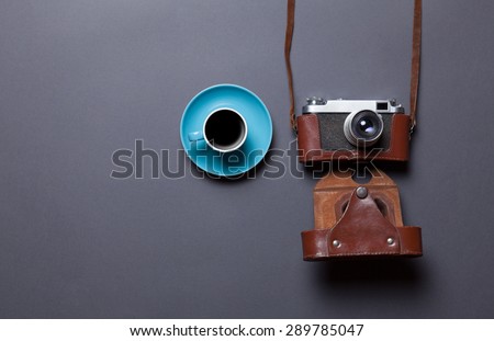 blue cup of coffee and retro camera in leather case on grey background