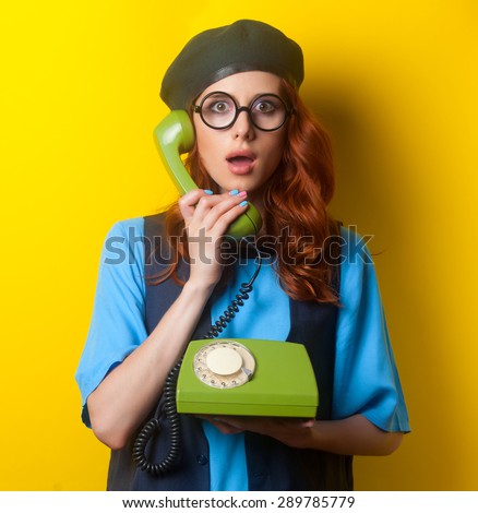 Surprised redhead girl with dial phone on yellow background.