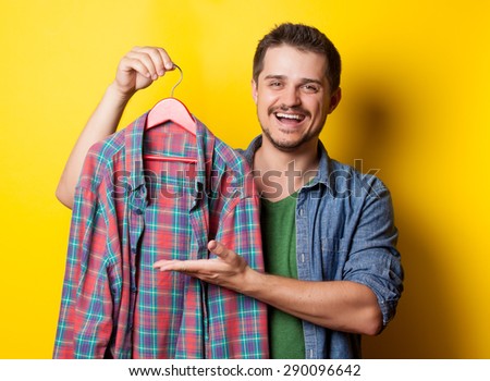 young smiling guy with hanger and shirt on yellow background.